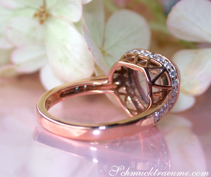Rosenquarz Herz-Ring mit Brillanten in Roségold, Detailaufnahme, blühende Blume im Hintergrund.