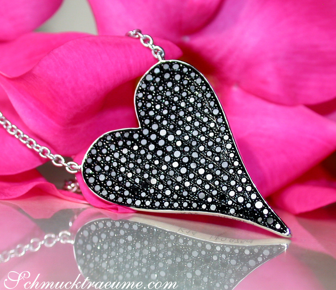 Herz-Anhänger aus Weißgold mit schwarzen Diamanten auf rosa Blüte, Detailaufnahme.