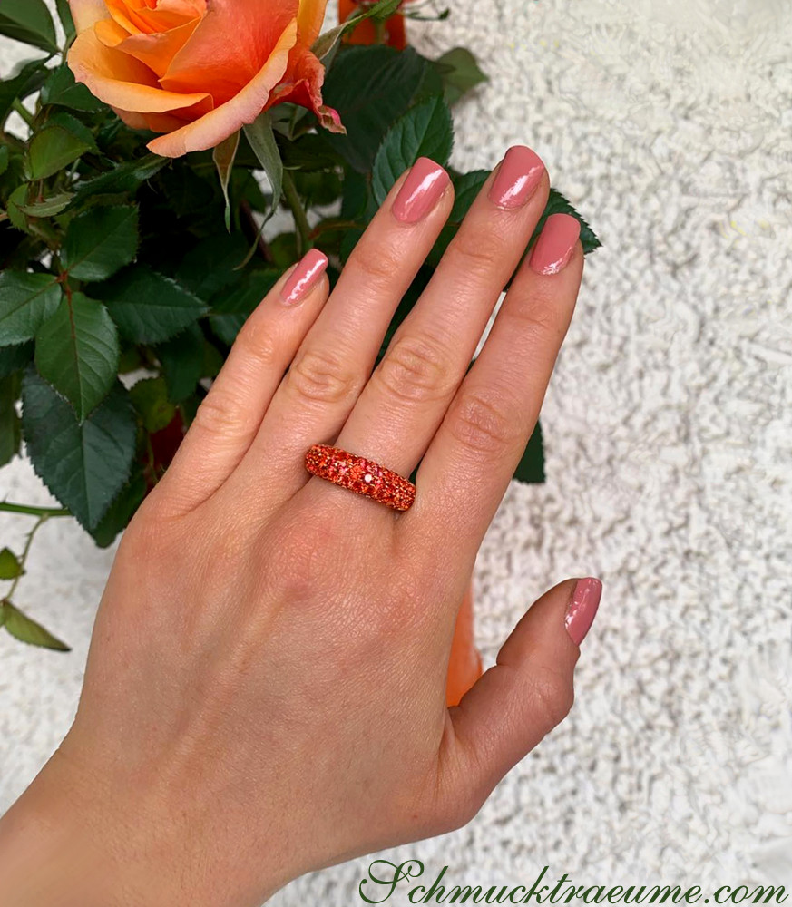 Rosa Nagellack auf Hand vor Rosenpflanze, Ring mit orangefarbenem Saphir-Pavé
