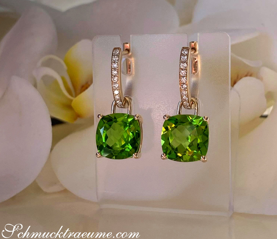 Peridot-Kissen-Ohrringe aus Gelbgold 585, detailreich verziert mit Diamanten, vor weißem Blütenhintergrund.