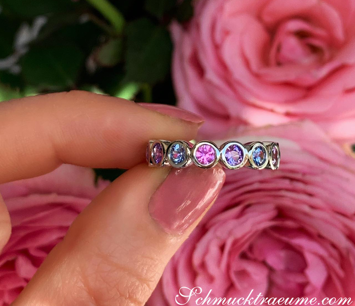 Memory Ring aus Weißgold mit Saphiren in Pastellfarben, vor rosa Rose