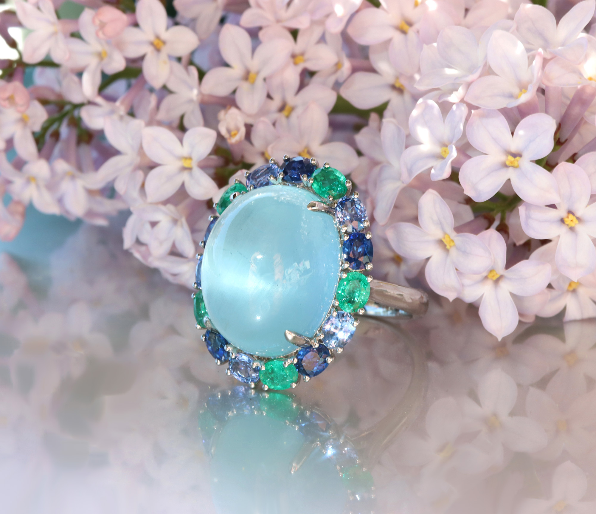 Milky Aquamarin-Ring mit Saphiren und Smaragden auf Lilienblüten.
