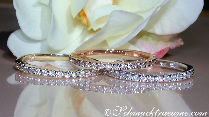 Detailansicht von drei Diamantringen aus Weiß-, Gelb- & Roségold, zarte Struktur, reflektierendes Untergrundlicht