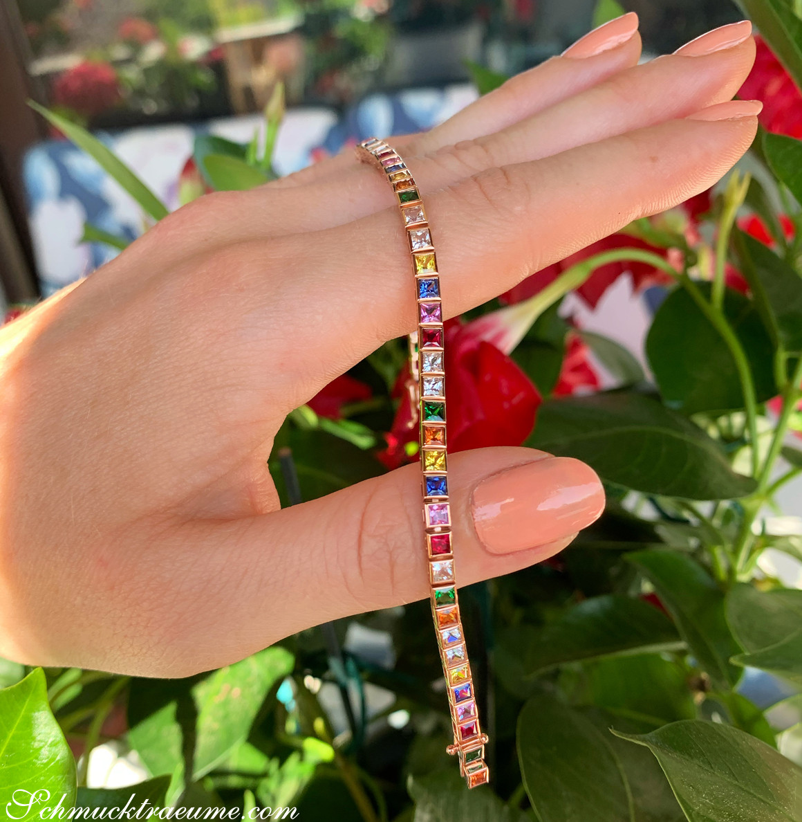 Hand mit prächtigem Multicolor-Saphir-Armband vor Blumen