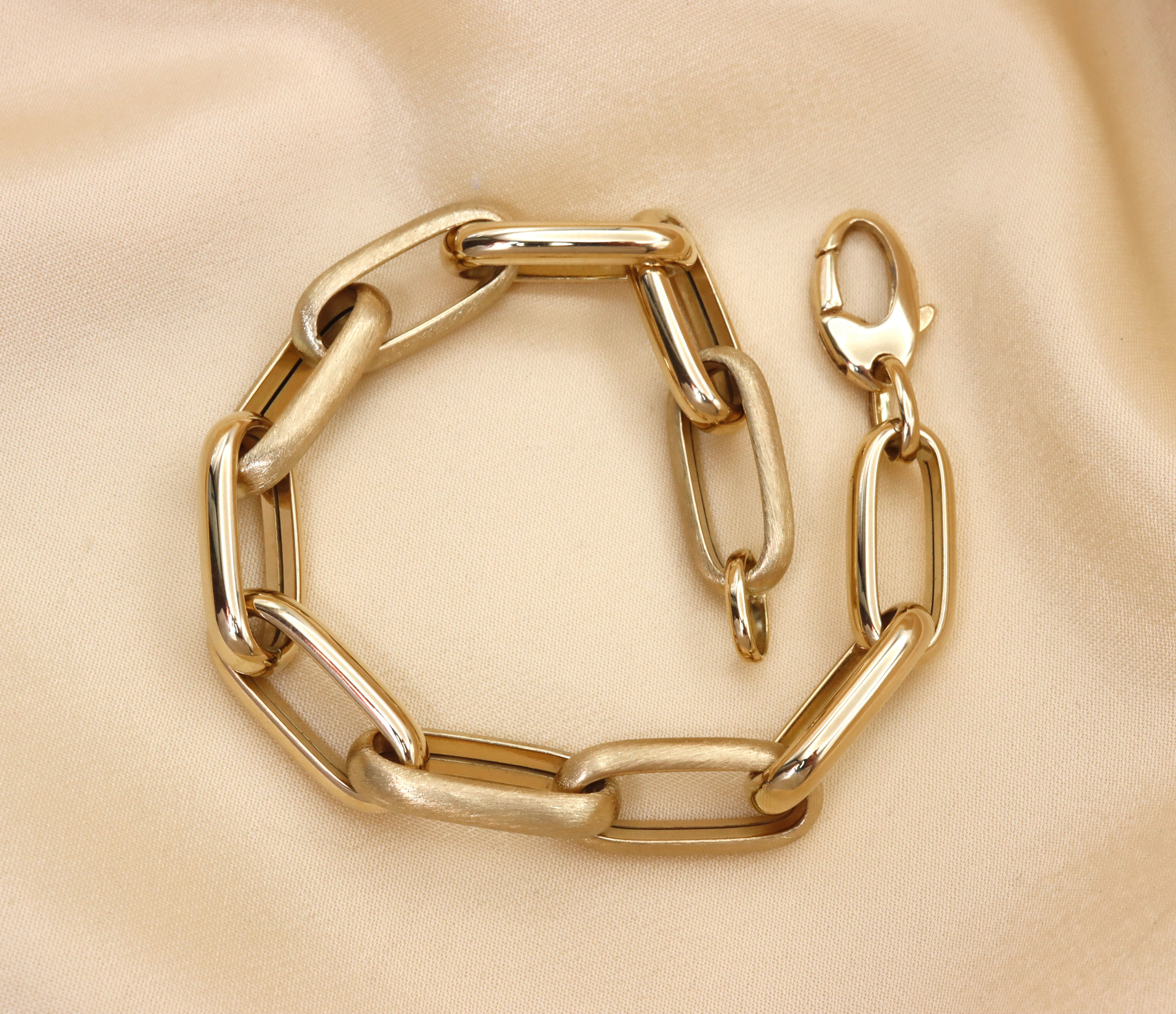 Gold-Paperclip-Armband in 585er Gelbgold, hochglänzend und satiniert, auf cremefarbenem Stoff liegend.