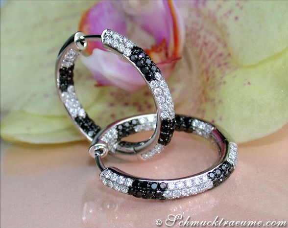 Schwarz-weiße Diamant-Creolen auf Hand, Blüte im Hintergrund