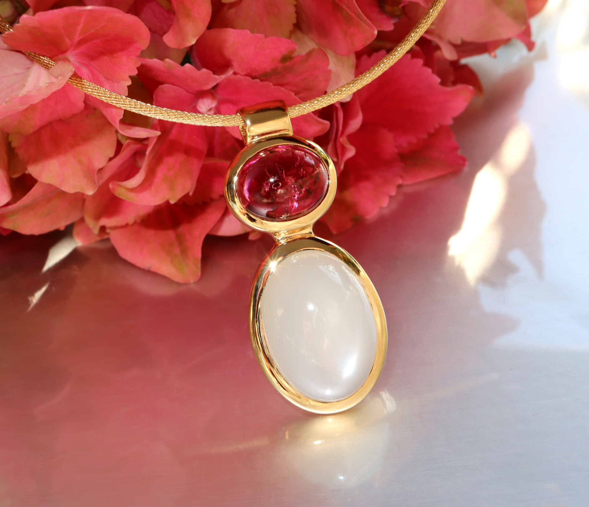 Goldene Halskette mit Rubellit und Mondstein vor rosa Blüten