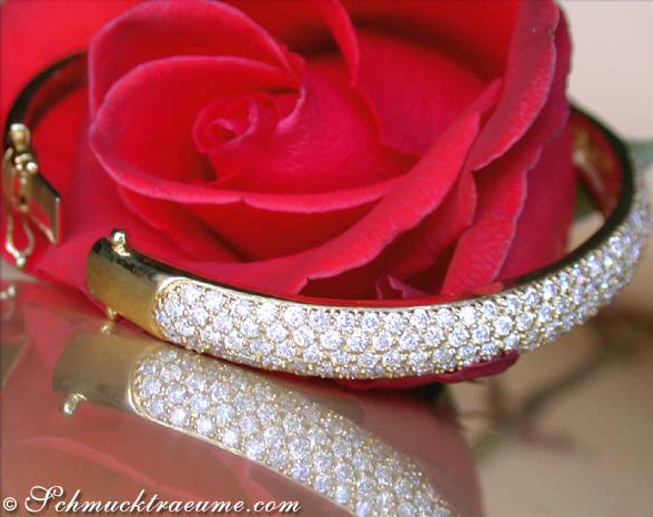 Gelbgold-Armreif mit Diamanten, Detailaufnahme, rosafarbene Rose im Hintergrund