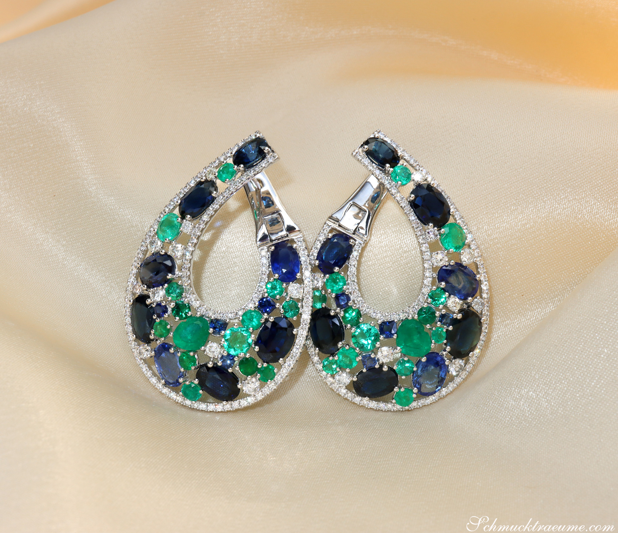 Weißgold-Ohrringe mit Saphiren, Smaragden und Diamanten, elegant auf Satin ausgelegt