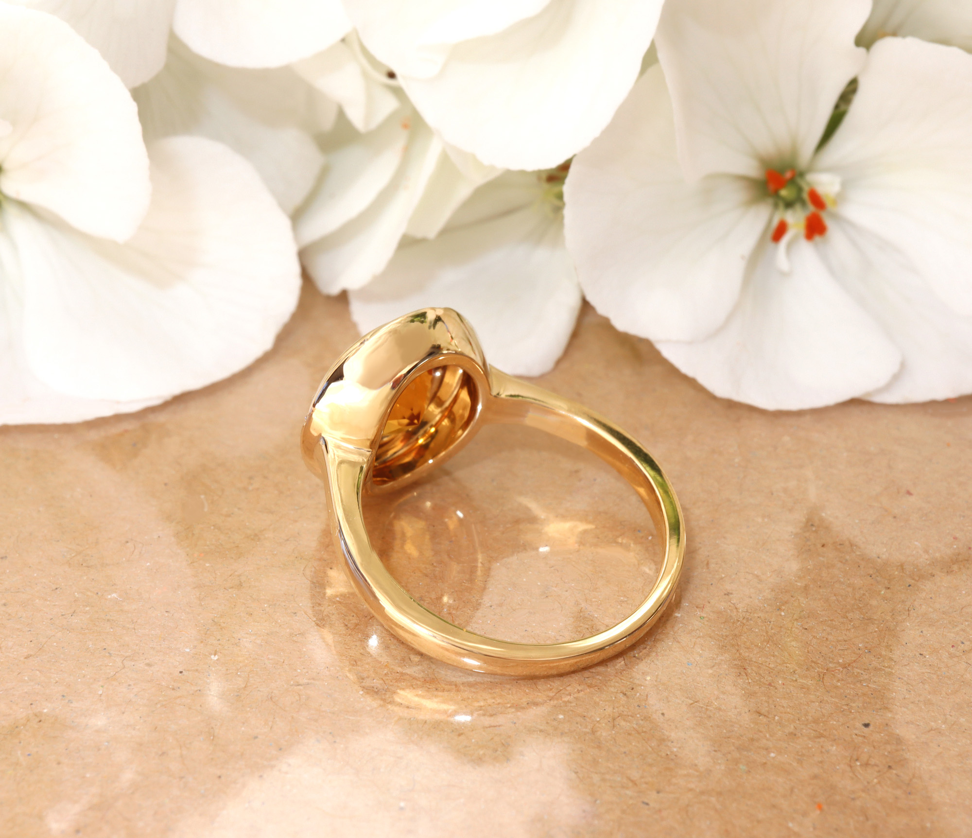 Goldener Citrin-Ring mit Brillanten vor weißen Blüten.