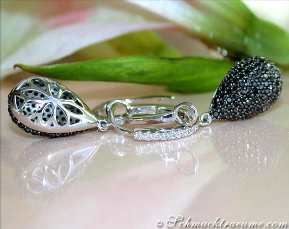 Schwarze Diamant-Ohrringe aus Weißgold, Detailansicht, glänzende Perlen, eleganter Design, auf grünem Blatt Hintergrund.