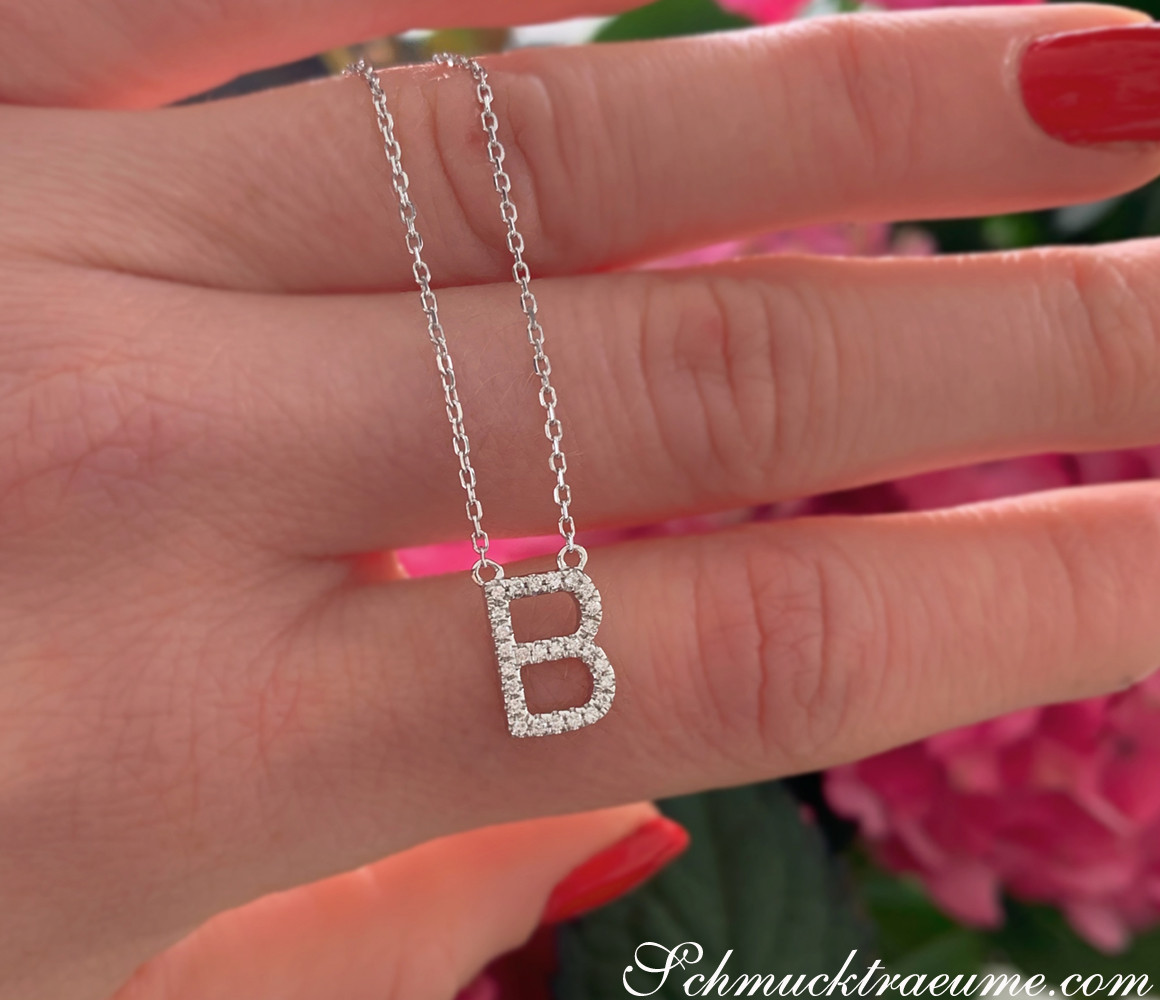 Hand zeigt zarte Halskette mit Brillanten-Initiale 'B', Detailaufnahme