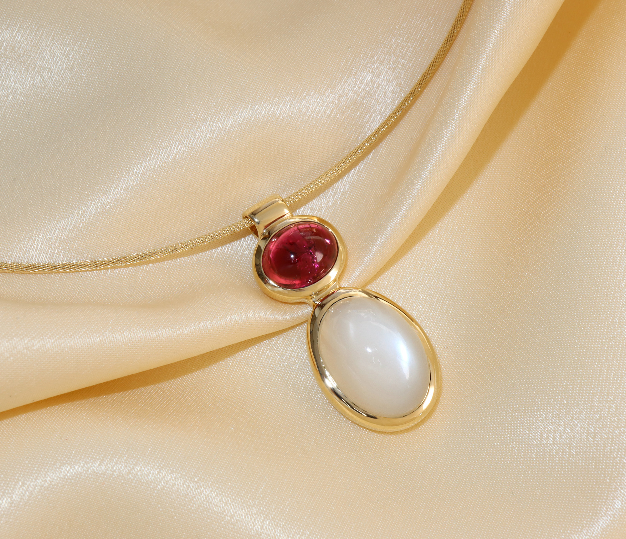 Goldene Halskette mit Rubellit und Mondstein, detailreich, elegant, auf cremefarbenem Stoff.