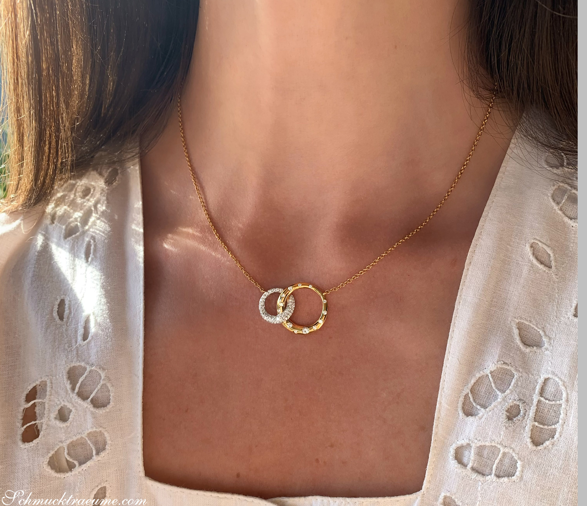 Goldene Halskette mit zwei ineinanderliegenden Ringen, strahlend glänzende Brillanten, getragen über zarter Spitze.