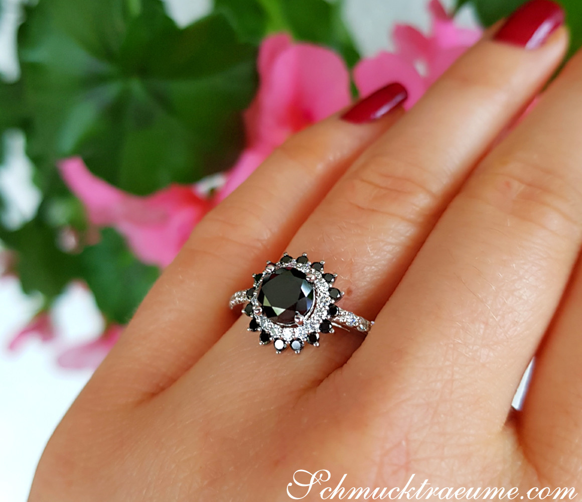 Schwarzer Diamant Solitär-Ring auf Hand mit rotem Nagellack, Hintergrund mit Blüten.