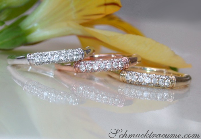 Drei Diamantringe im Bambus Design auf glänzender Oberfläche, Blume im Hintergrund.