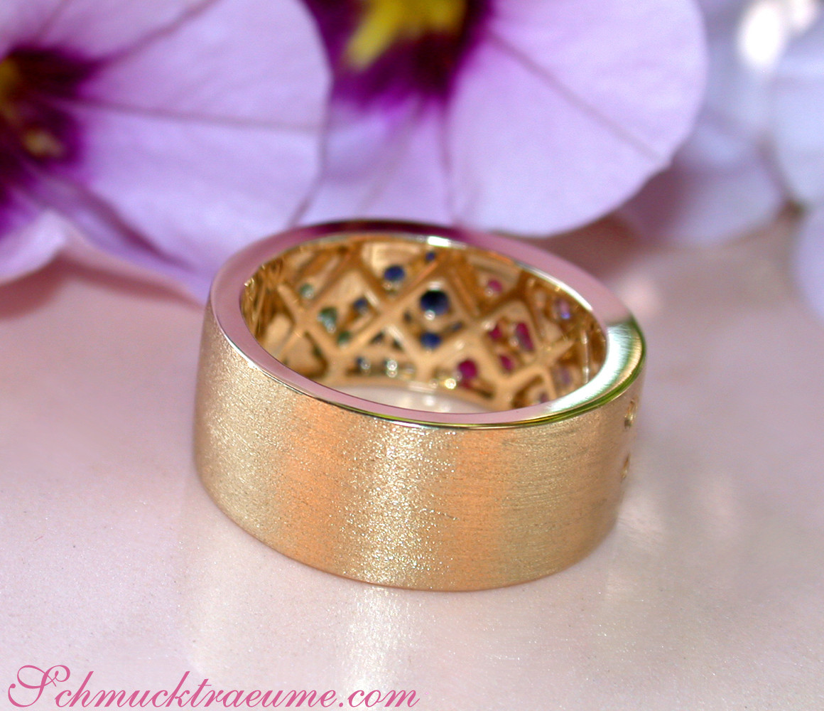 Goldener Ring mit satiniertem Finish und farbigen Steinen, Detailaufnahme vor Orchidee.