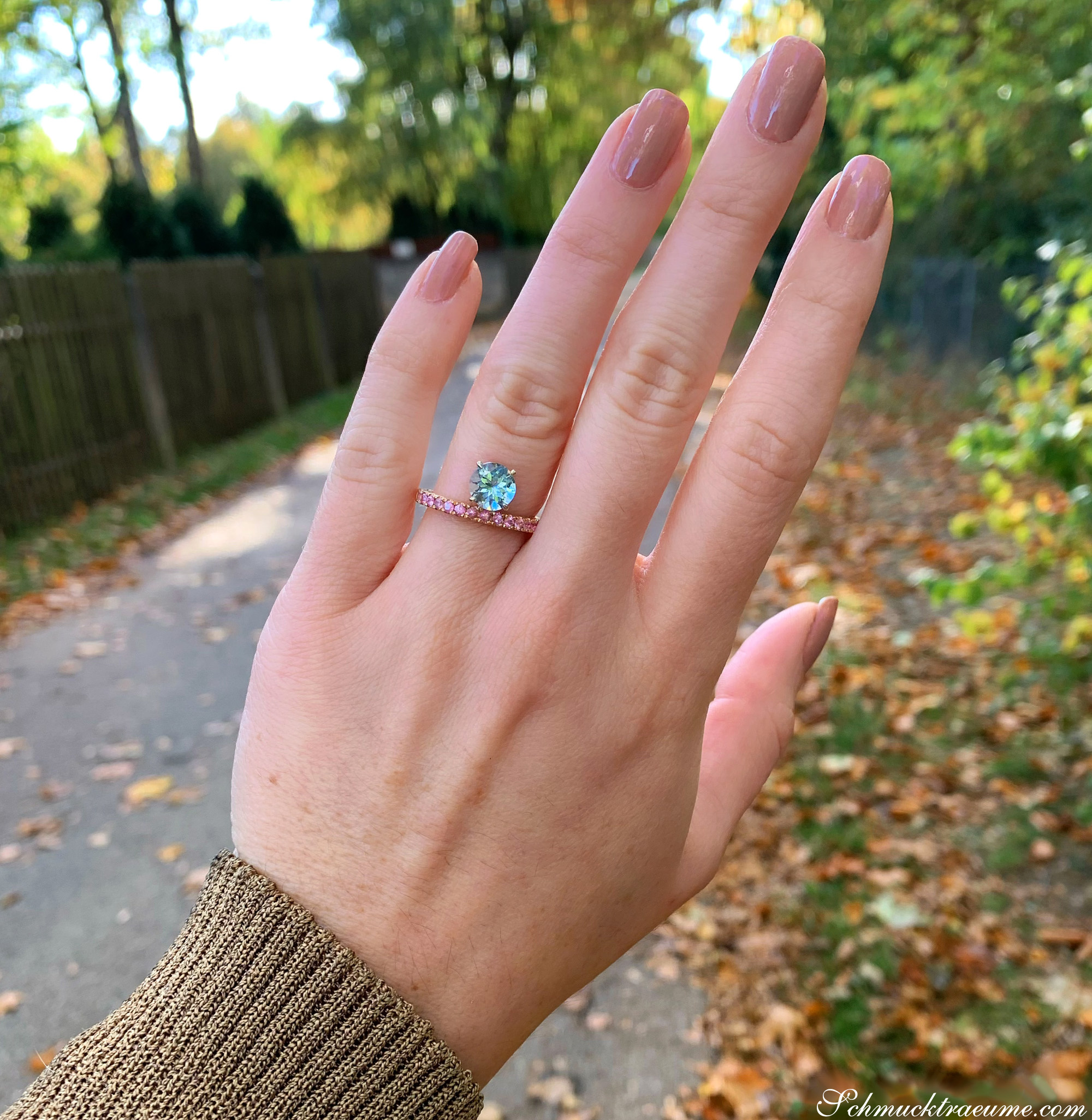 Nahaufnahme von Aquamarin-Ring mit rosa Saphiren auf Hand vor Herbstlandschaft.