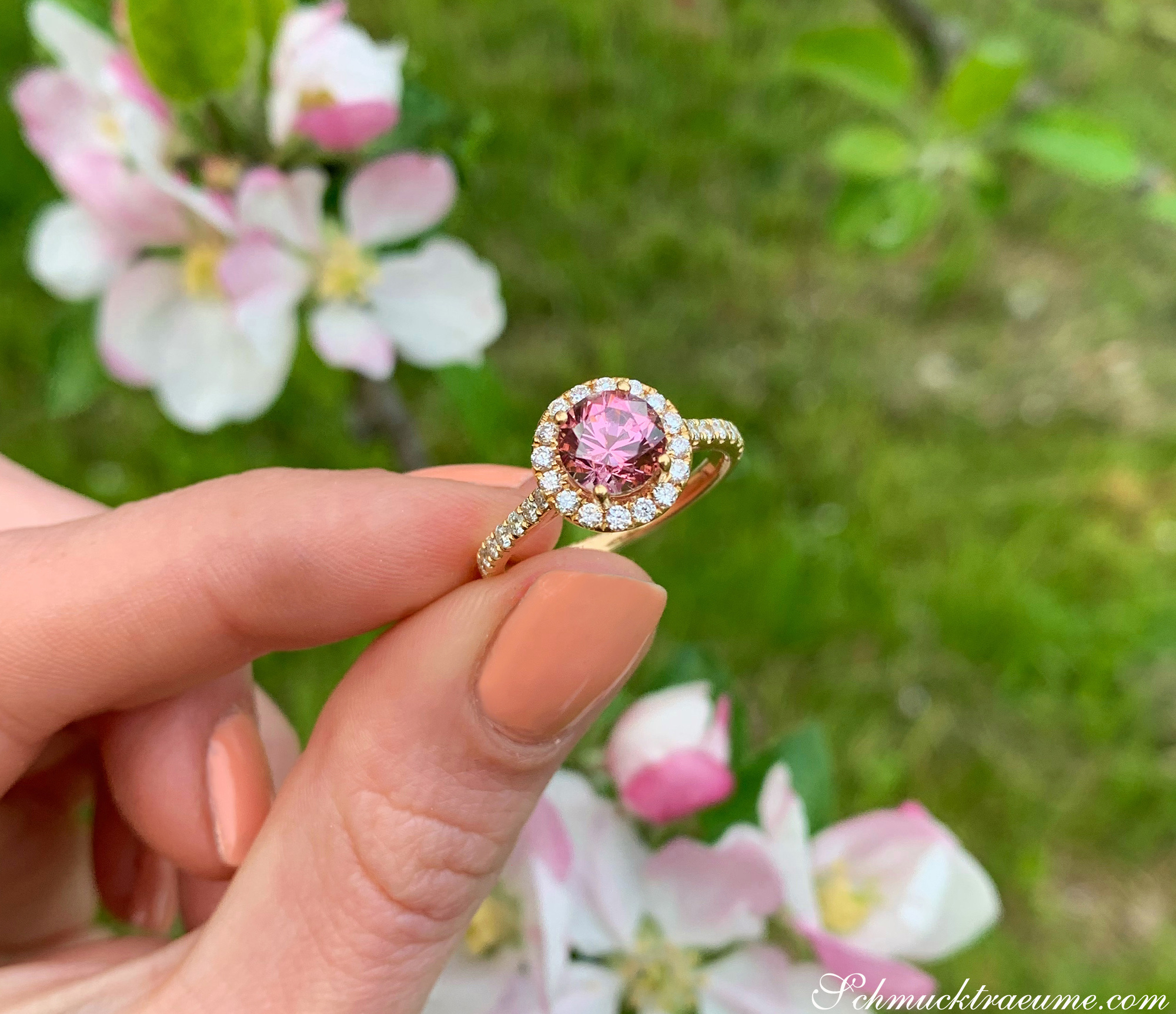 Femininer Malaya Granat Ring mit Brillanten in Altrosa, Gelbgold 750, im Frühlingsambiente mit Blüten.