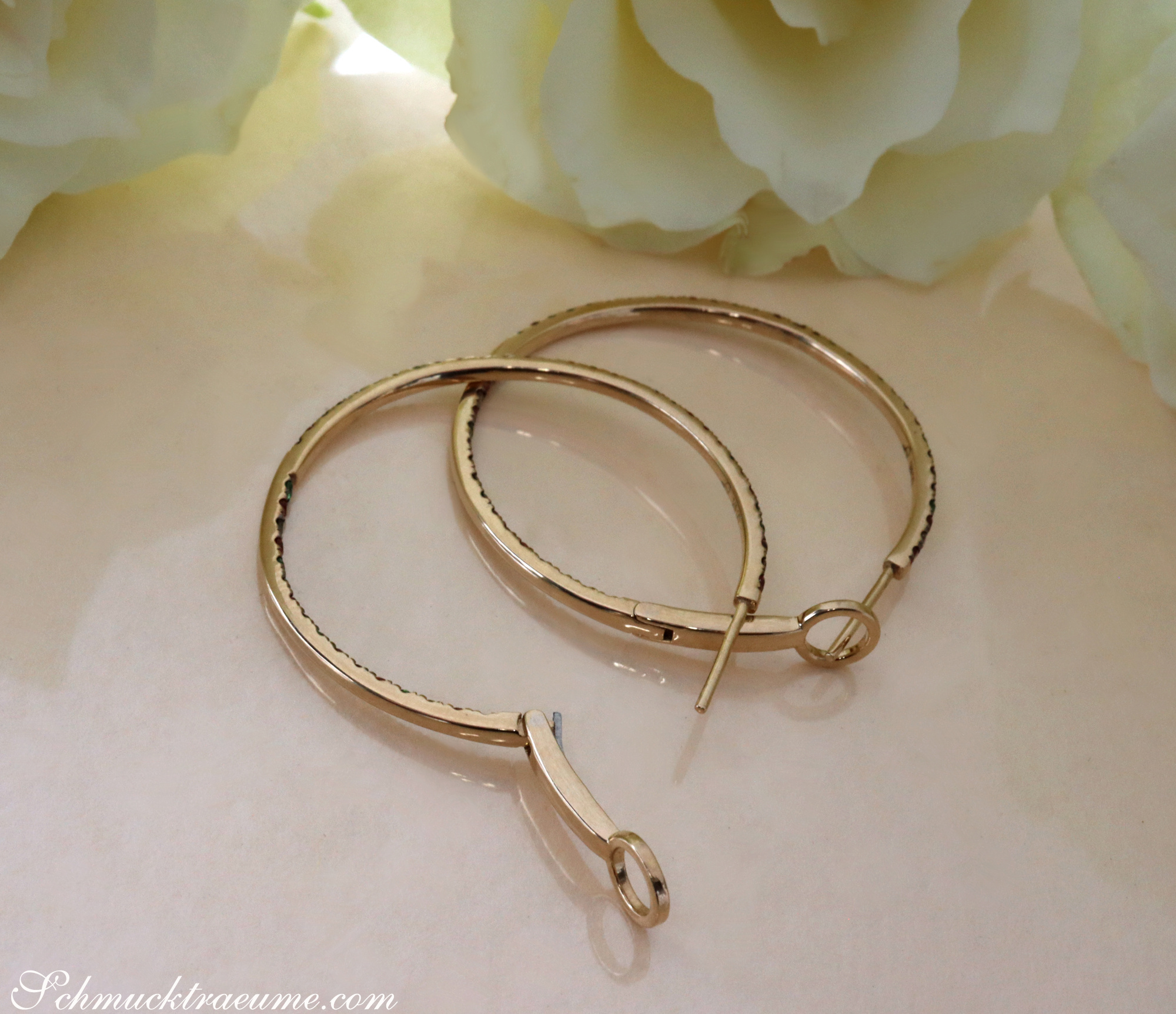 Goldene Creolen mit Diamanten und Saphiren auf weißem Hintergrund