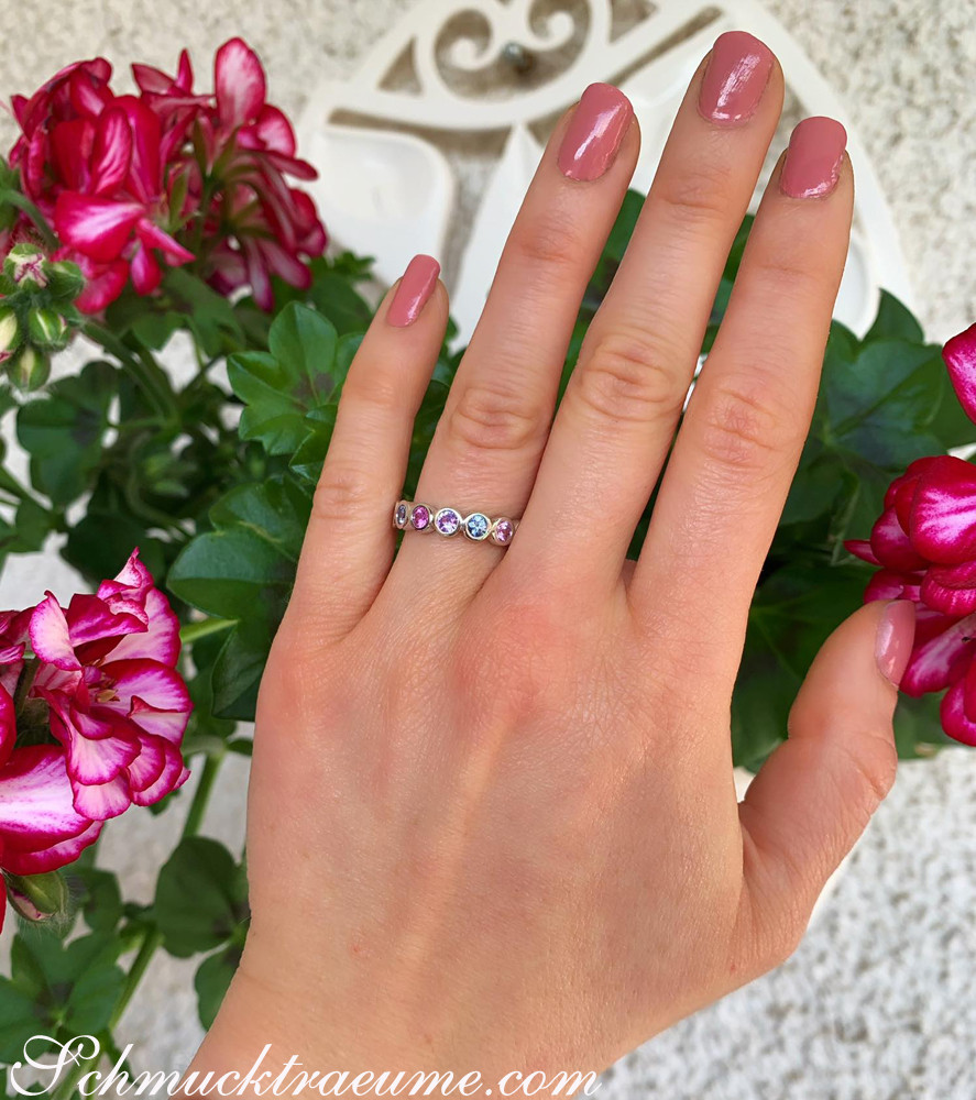 Memory-Ring mit Saphiren in Pastellfarben, Nagellack rosa, Blumen im Hintergrund