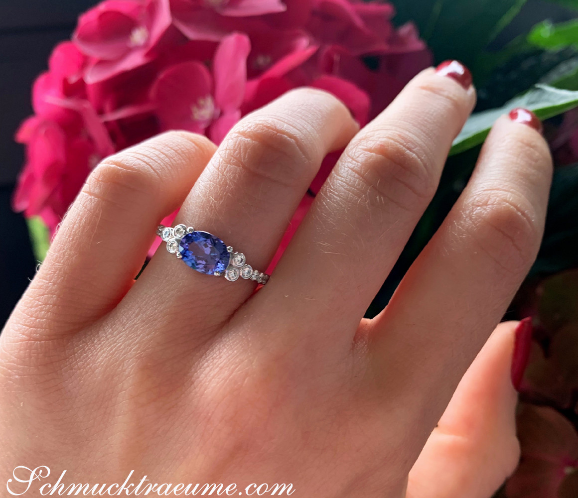 Weißgoldring mit Tansanit und Diamanten, vor Blumenblüten.