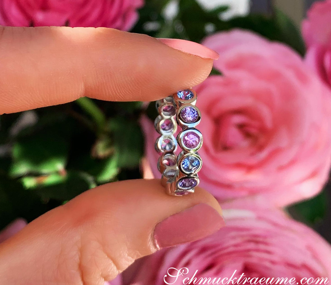 Memory-Ring mit Saphiren in Pastellfarben auf Finger, Rosen im Hintergrund
