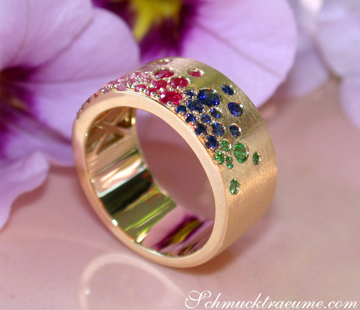 Goldener Ring mit Saphiren, Rubinen und Tsavorites, satiniert, Detailaufnahme, vor Blütenblättern