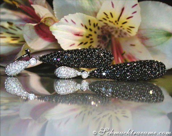 Schwarze Diamanten-Ohrgehänge auf glänzender Oberfläche, Blüten im Hintergrund