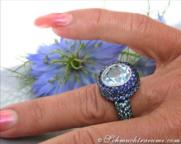 Blautopas-Ring mit Saphiren, Detailaufnahme auf blauem Blütenhintergrund