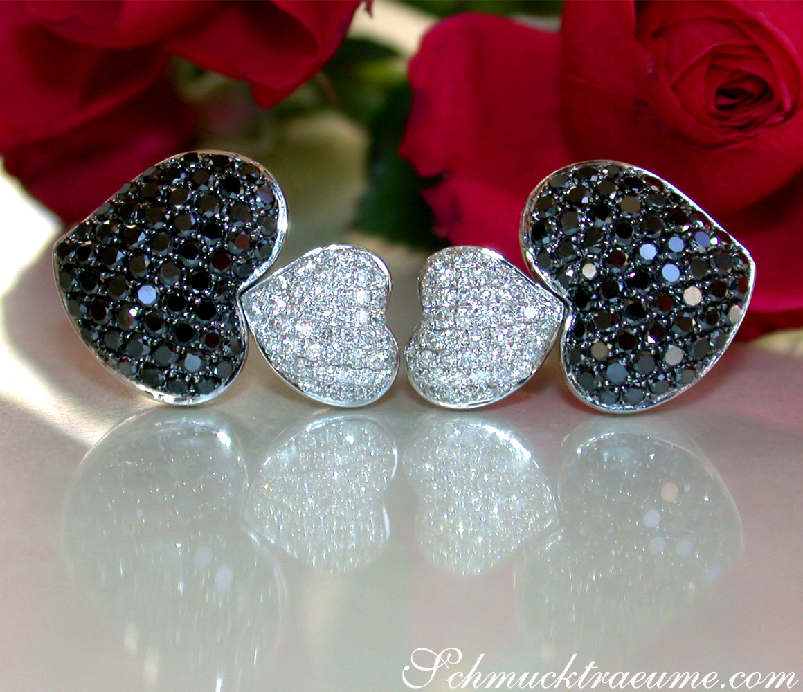 Raffinierte Herz-Ohrstecker mit schwarzen und weißen Diamanten, vor Rosenblüten.