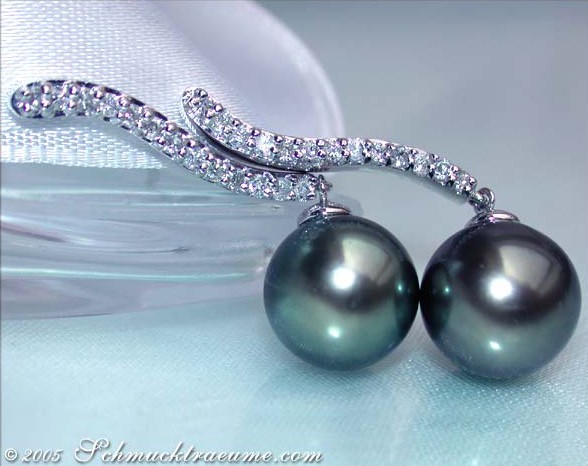 Tahitiperlen-Ohrringe mit Brillanten auf weißem Stoff, elegante Linien und Perlendurchmesser 10-11 mm.