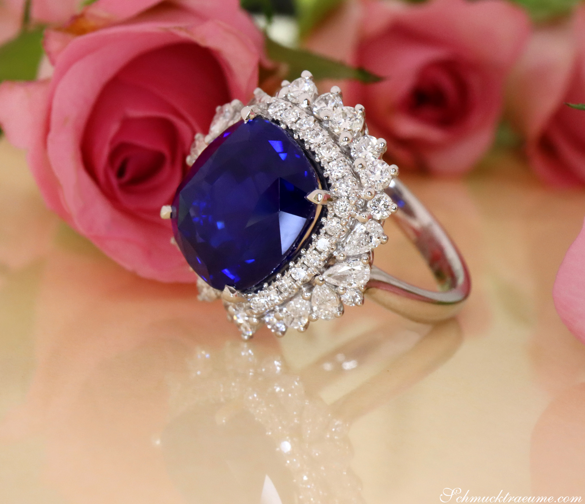 Blauer Ceylon-Saphir-Ring mit Diamanten in Weißgold, vor Rosenblüten.