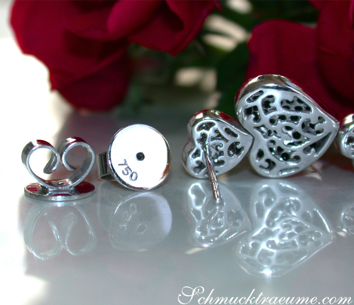 Silberne Herz-Ohrstecker mit filigranem Muster, rosafarbene Blume im Hintergrund