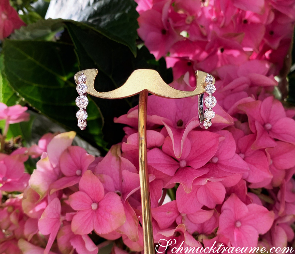 Goldene Creolen mit drei Brillanten auf Blütenhintergrund