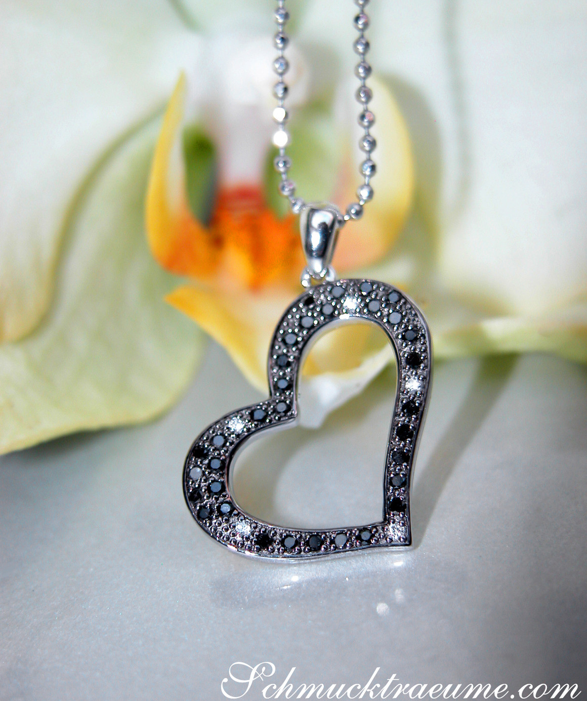 Schwarzer Diamanten Herz-Anhänger auf Kette, im Hintergrund Blume