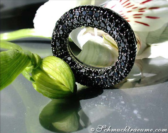 Schwarzer Diamantenkreisanhänger im Detail, umgeben von Orchideenblättern.