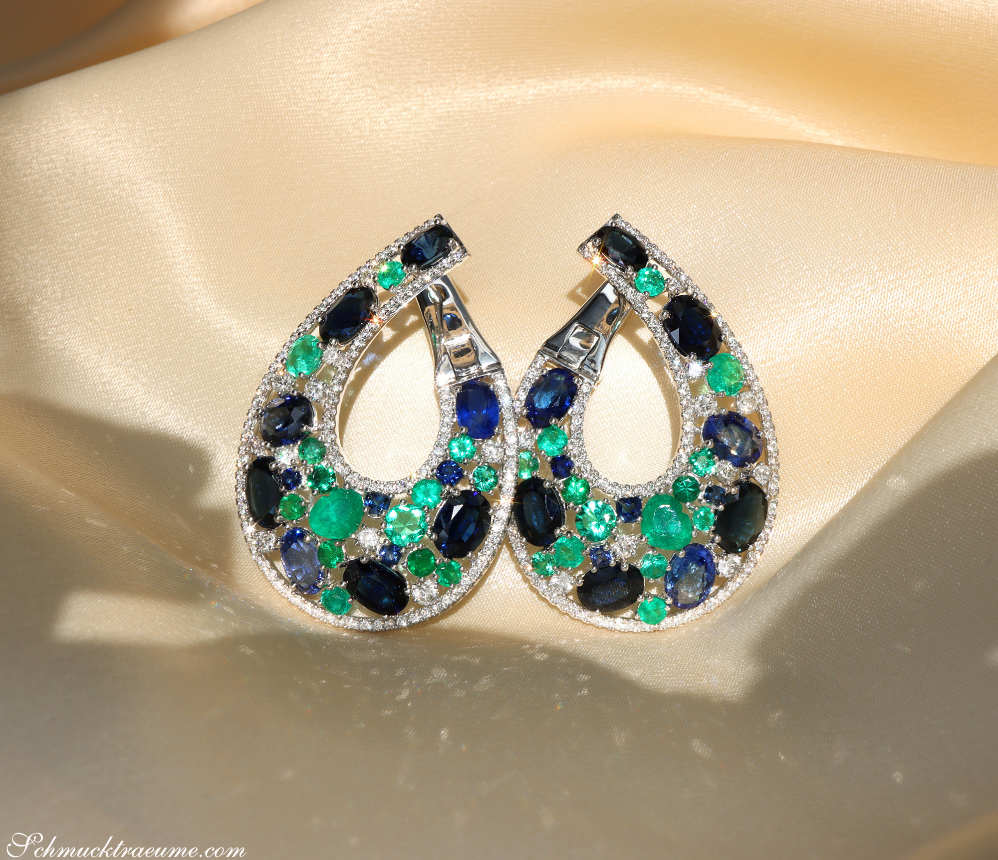 Teilansicht von Saphir-Ohrgehängen mit Smaragden und Diamanten auf cremefarbenem Stoff