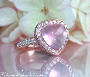 Cabochon-Rosenquarz Herz-Ring mit Brillanten, roségold, Detailaufnahme, blühende Blüten im Hintergrund.