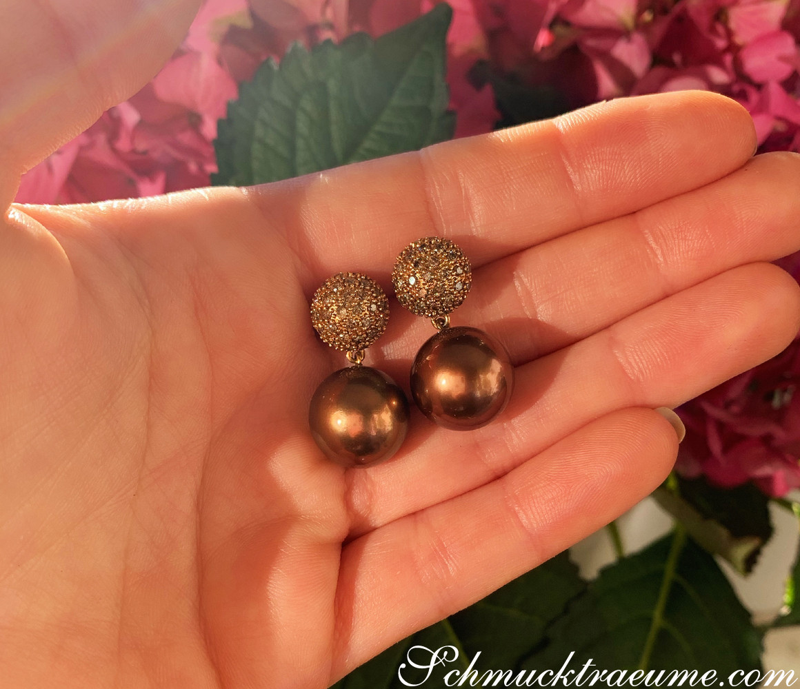 Bronze-Tahitiperlen-Ohrstecker mit naturbraunen Brillanten auf Handfläche, Detailaufnahme.