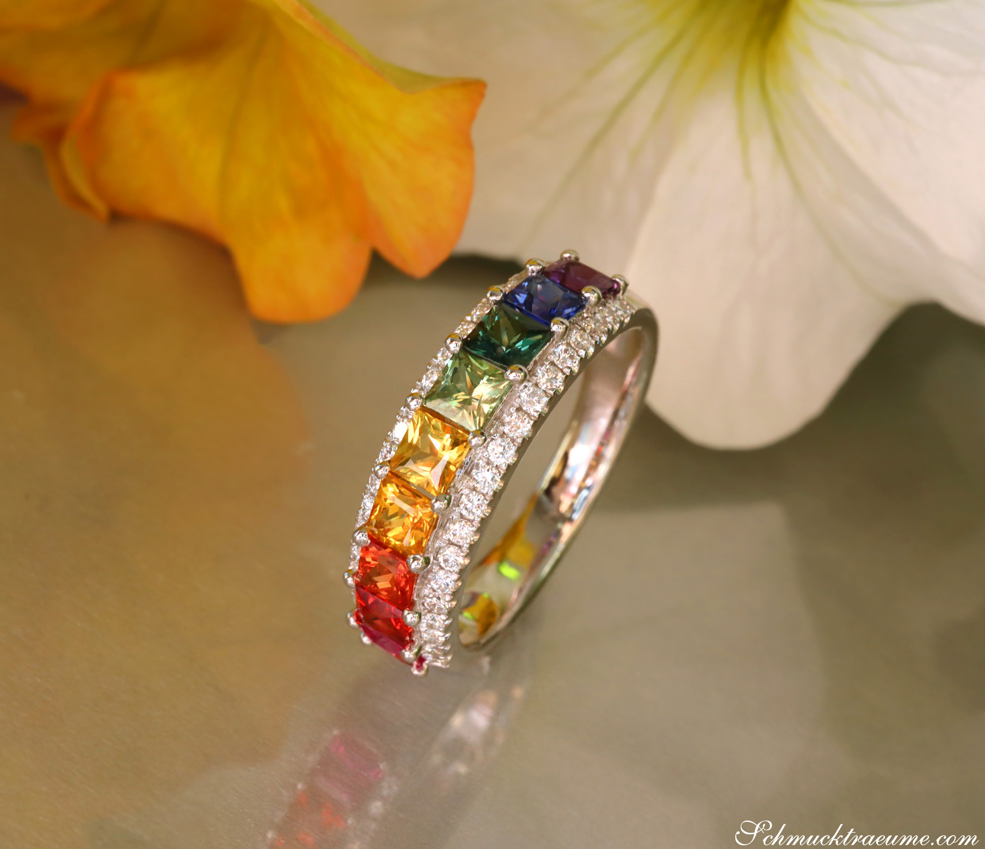 Weißgold-Ring mit Regenbogen-Saphiren und Brillanten, Detailaufnahme, Blüten im Hintergrund.