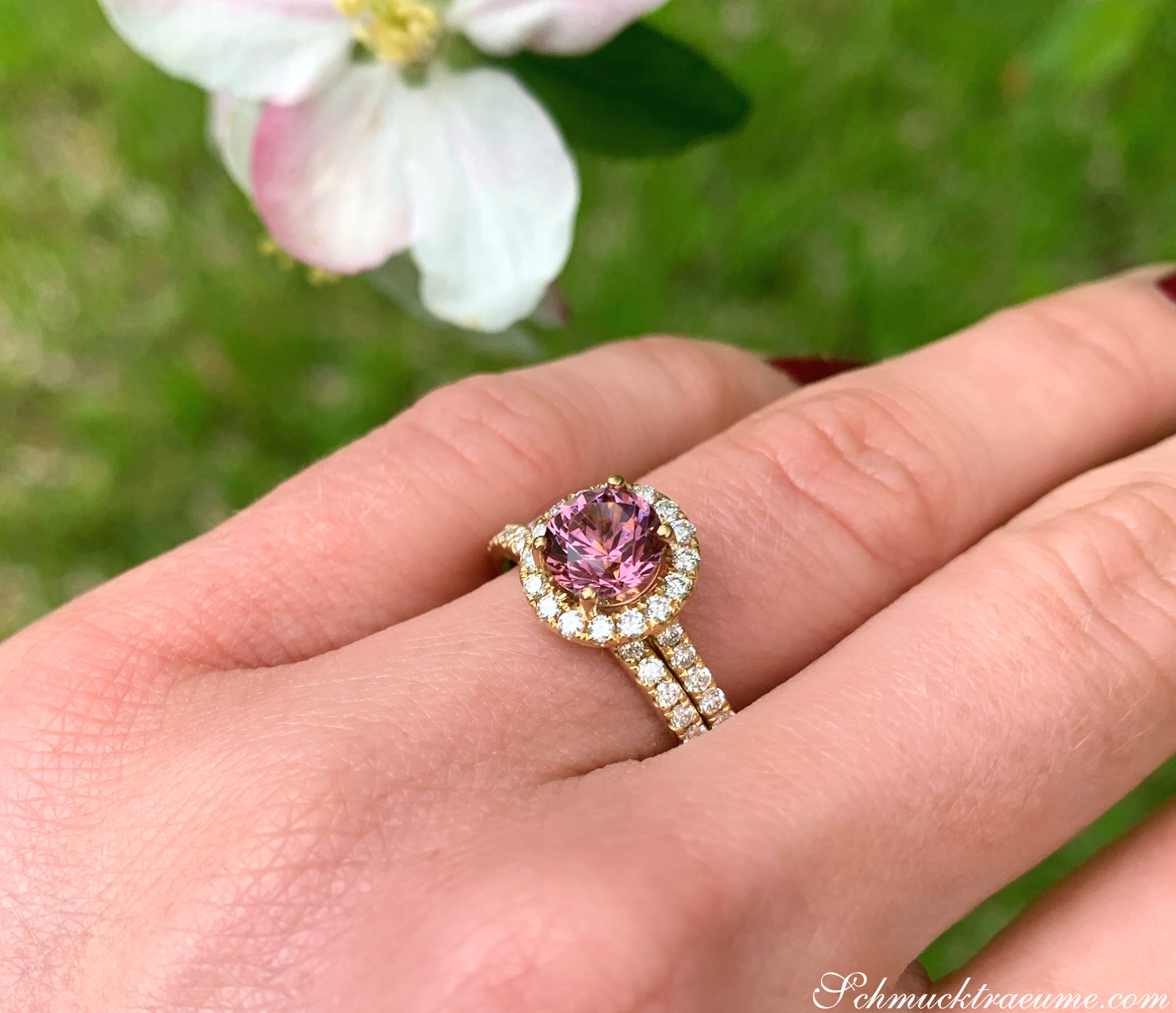 Finger mit rosa Granat-Ring mit Diamanten, Hintergrund mit Blume.