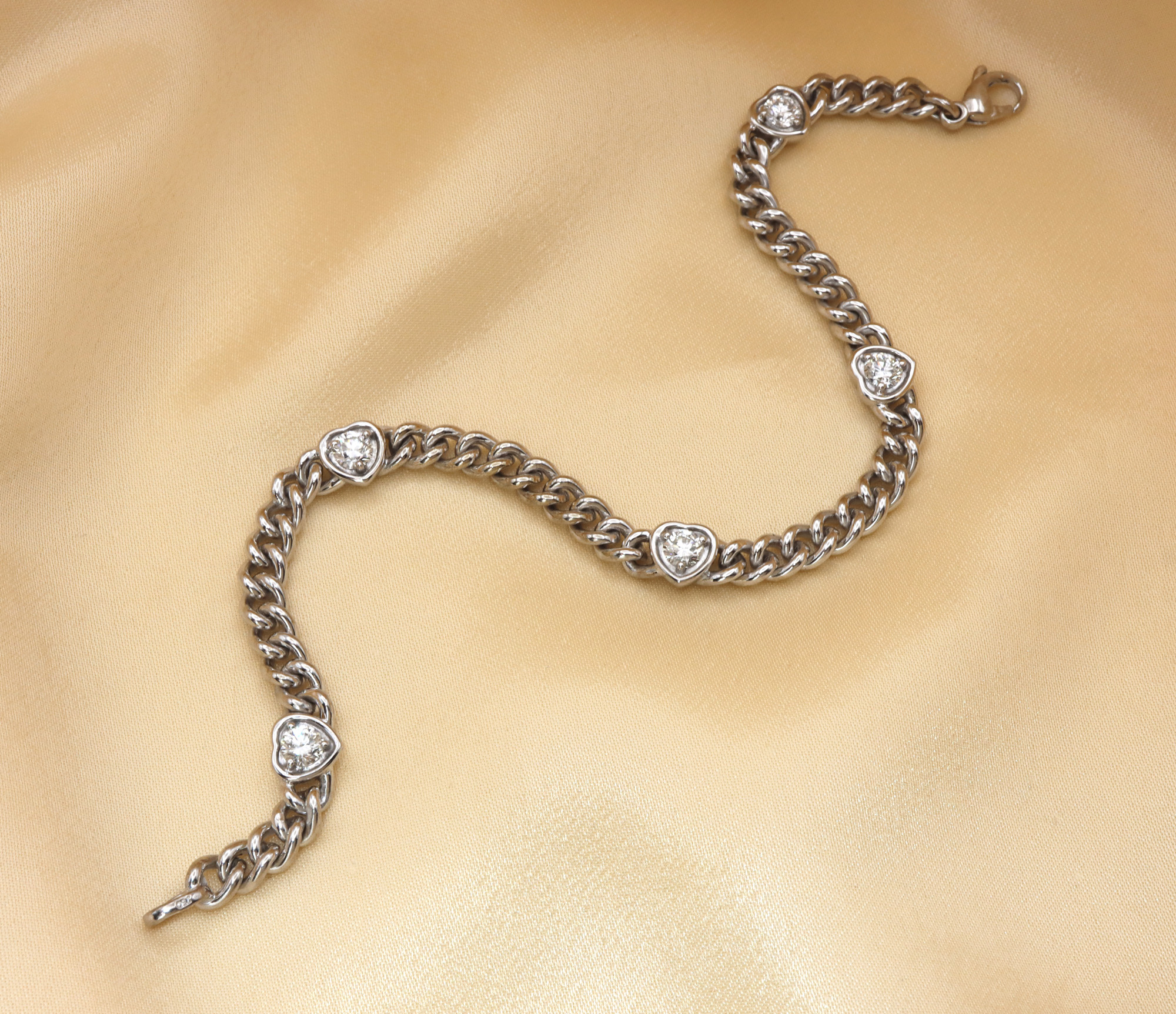 Silbernes Panzerarmband mit Brillantenherzen auf cremefarbener Stoffoberfläche
