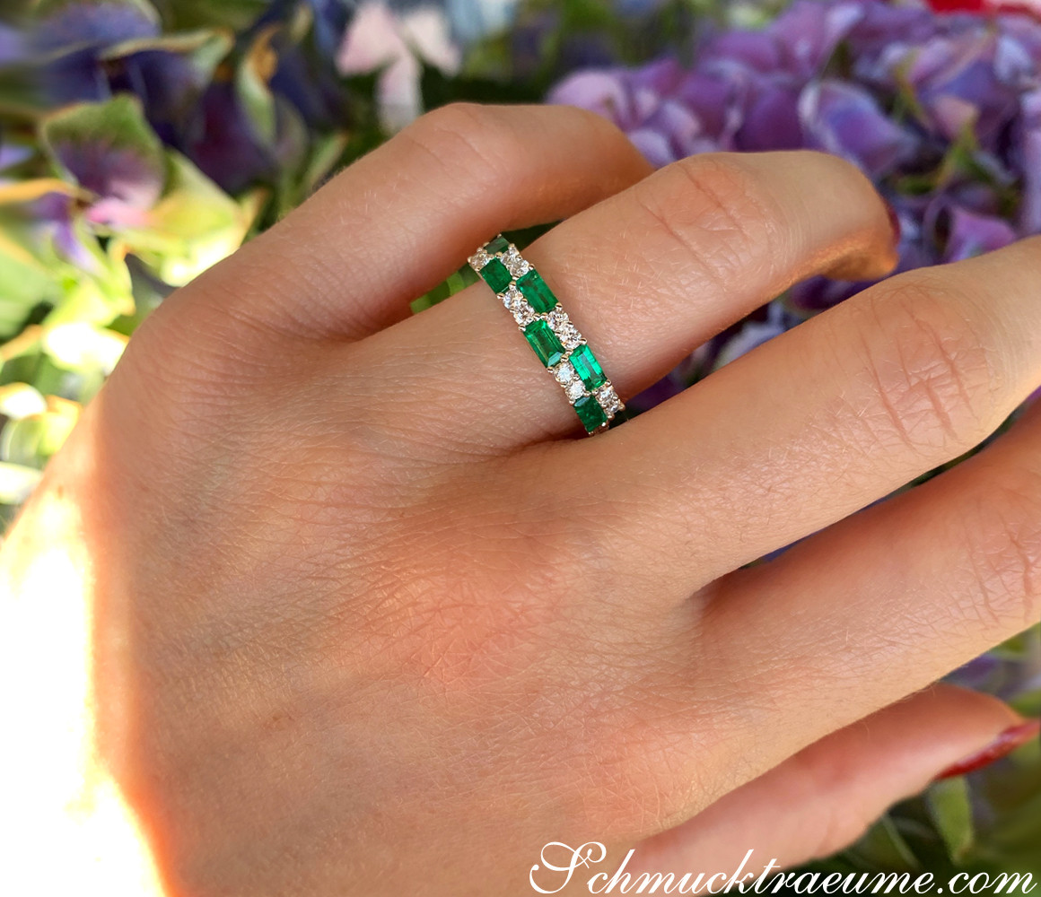 Hand mit Bandring aus Weißgold mit Smaragden und Brillanten, Hintergrund mit Blumen.