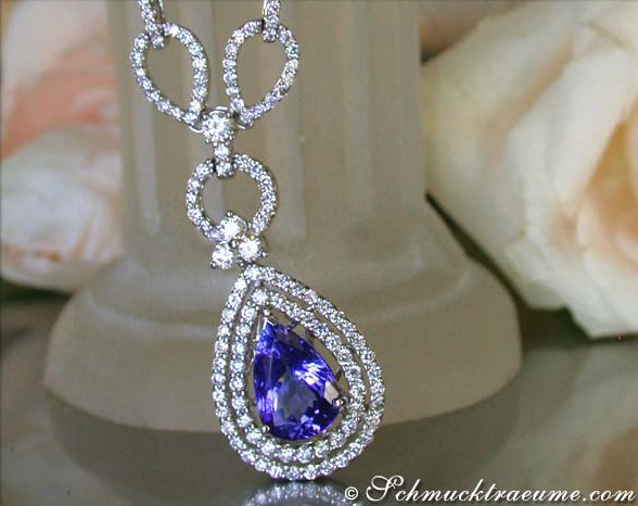 Weißgold-Collier mit Tansanit und Brillanten, detailreich verarbeitet, Rosen im Hintergrund.