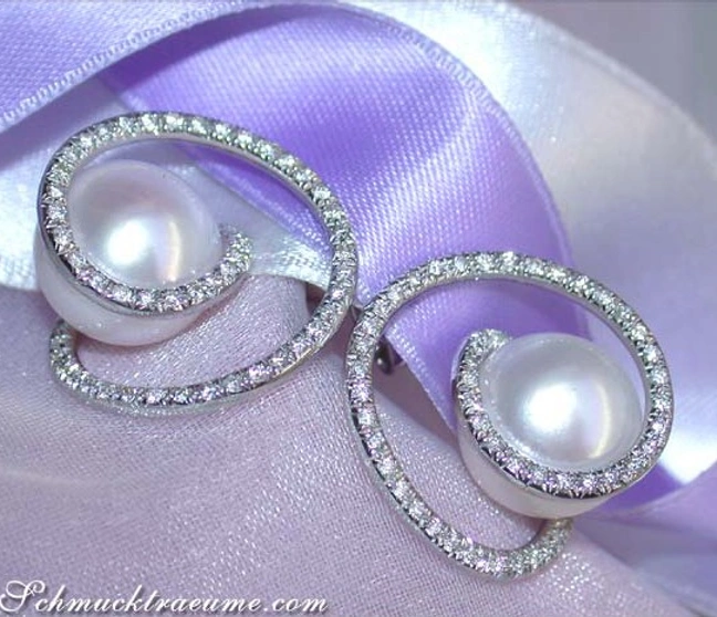 Südseeperlen-Ohrstecker mit Brillanten auf lila Satin, eleganter Schmuckdetail Südseeperlen-Ohrstecker mit Brillanten auf lila Satin, eleganter Schmuckdetail