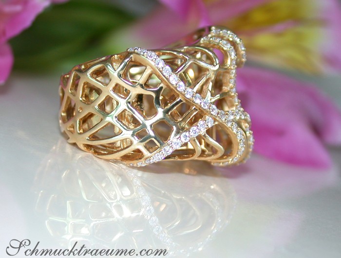 Goldener Brillantenring mit Diamanten, filigraner Netzstruktur, vor blühendem Hintergrund.