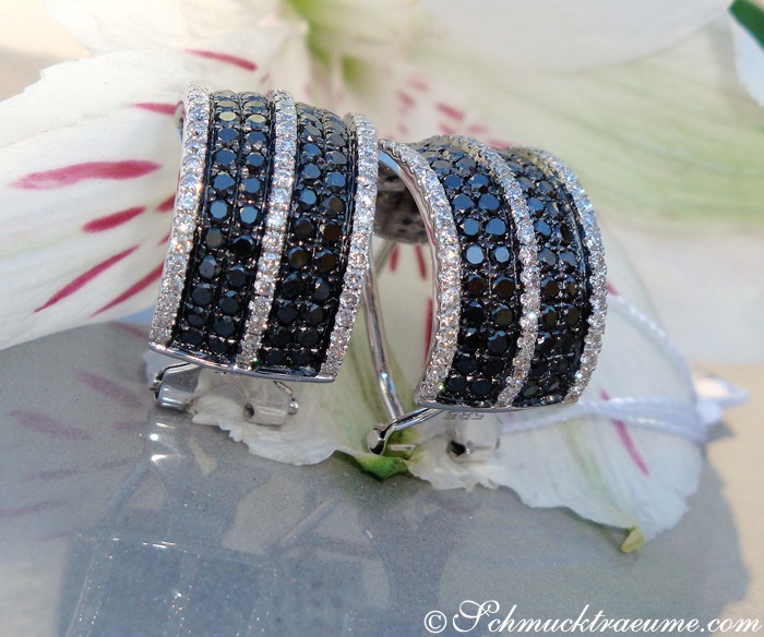 Detailaufnahme von Diamantohrringen mit schwarzen und weißen Diamanten auf Blütenblatt.