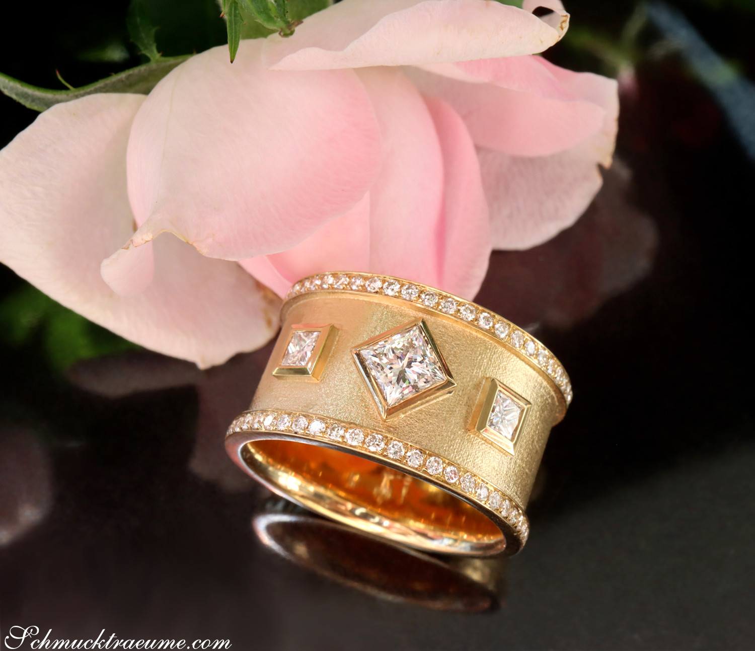 Goldener Diamant-Ring mit Princess-Diamanten und Diamantkranz, vor rosa Rose