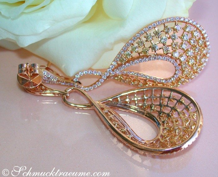 Goldene Ohrstecker mit weißen und gelben Brillanten, detailreich verziert, auf Rosenblüte gelegt